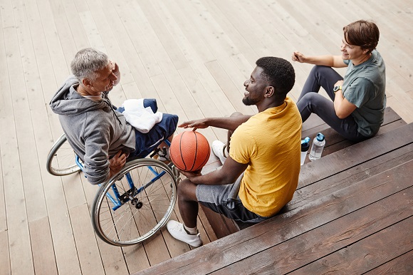 Das Bild zeig ein männliches Modell im Rollstuhl im Kreise von anderen Sportler*innen (Quelle: Foto (c) PantherMedia ) Das Bild zeig ein männliches Modell im Rollstuhl im Kreise von anderen Sportler*innen