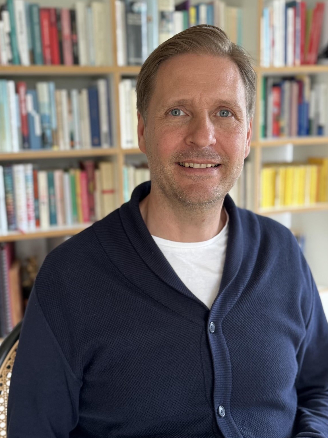Christian Eberhardt vor einem Bücherregal. (verweist auf: Christian Eberhardt unterstützt seit Februar 2024 das Team “Orchester” in München)