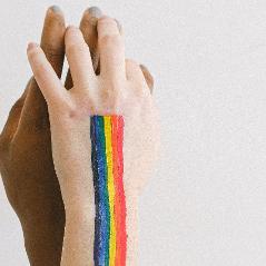 Das Bild zeigt sich umgreiende Hände. Auf dem vorderen Handrücken wurde ein Regenbogen gezeichnet. 